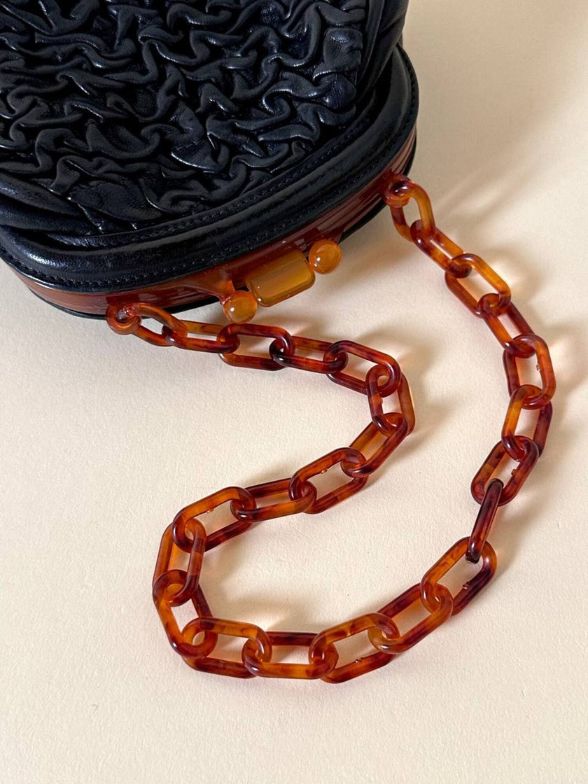 Borsa vintage in pelle nera goffrata con chiusura a scatto e catena in resina ambrata