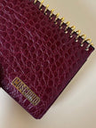 Pochette a quaderno in pelle bordeaux stampa coccodrillo “Moschino”